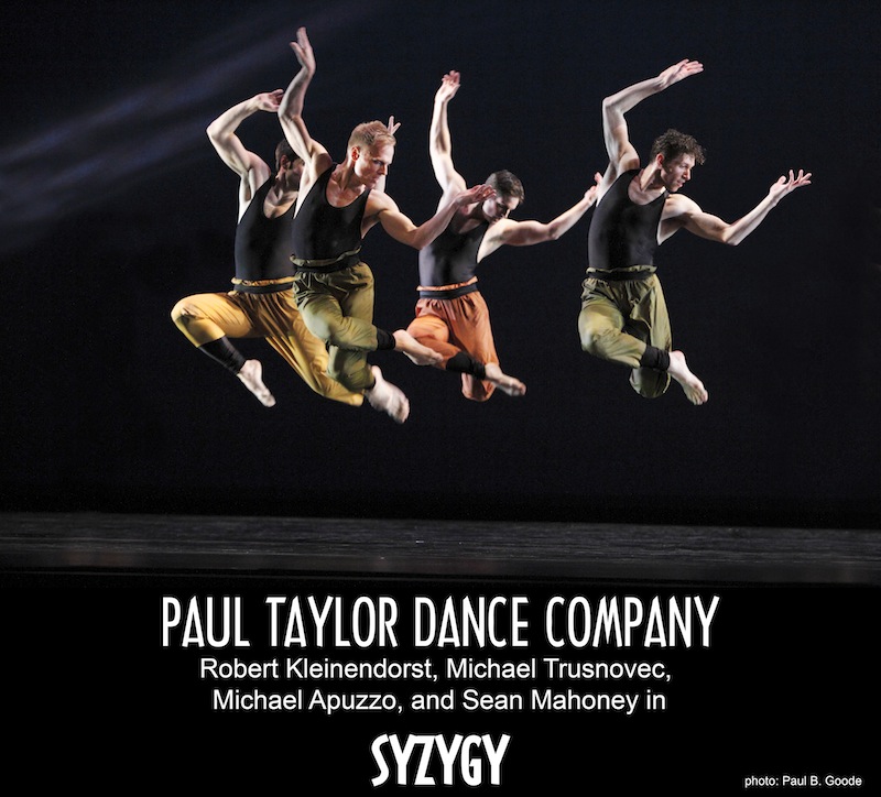 Four men in black muscle tanks with baggy pants leap in the air with crossed legs and their arms in ninety degree angles.